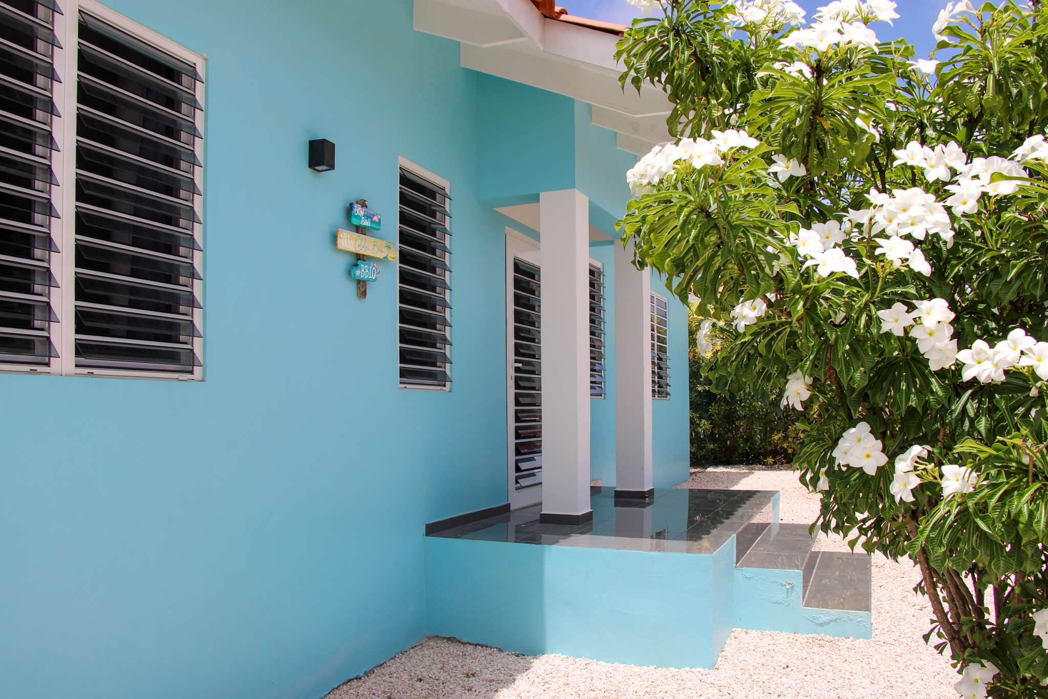 Front door of the villa with the name sign and a frangipani in bloom